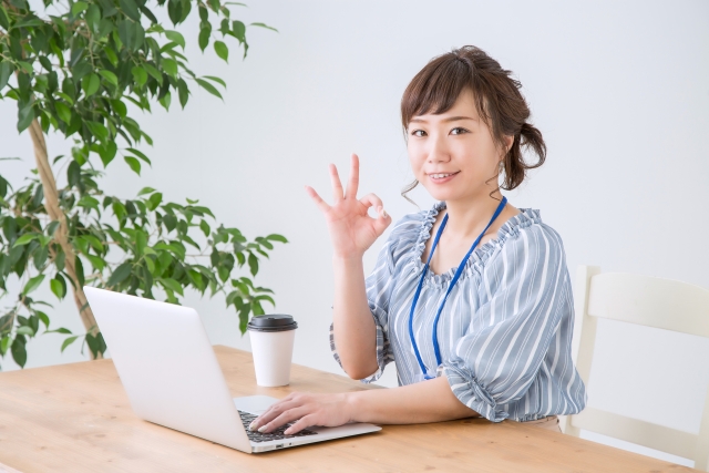 ノートパソコンを操作しながらOKサインをする女性